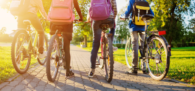 children from behind wearing backpacks on bicycles